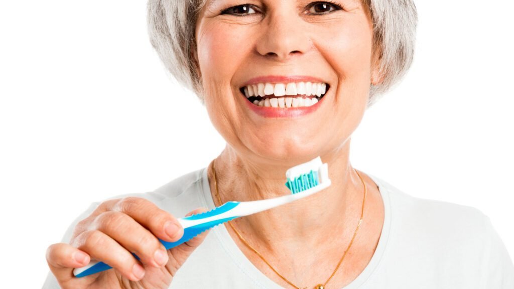 Adulta mayor sonriendo mientras se cepilla los dientes correctamente
