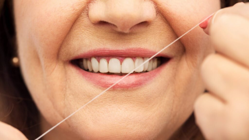 Adulta mayor sonriendo mientras usa la seda dental correctamente