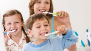 Madre e hijos sonriendo mientras cepillan sus dientes de forma correcta